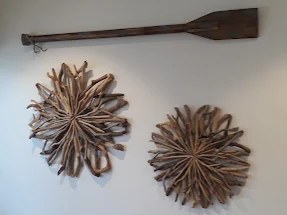 Large driftwood wall sculptures and a wooden oar mounted on a white wall